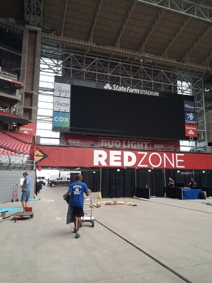 A Garcia mover wheeling a dolly across the floor of State Farm Stadium beneath the video board
