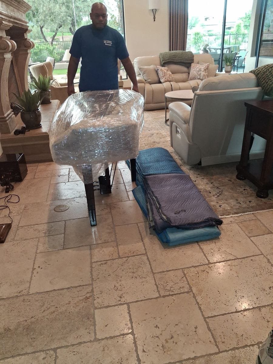 A Garcia mover guiding a shrink-wrapped piece through a living room, moving pads ready on the floor