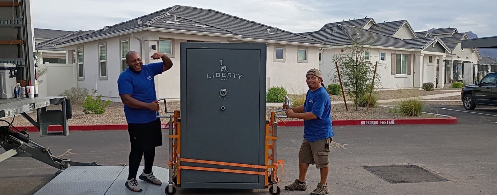 Two Garcia movers with a large gun safe strapped to a safe dolly at the truck's lift gate