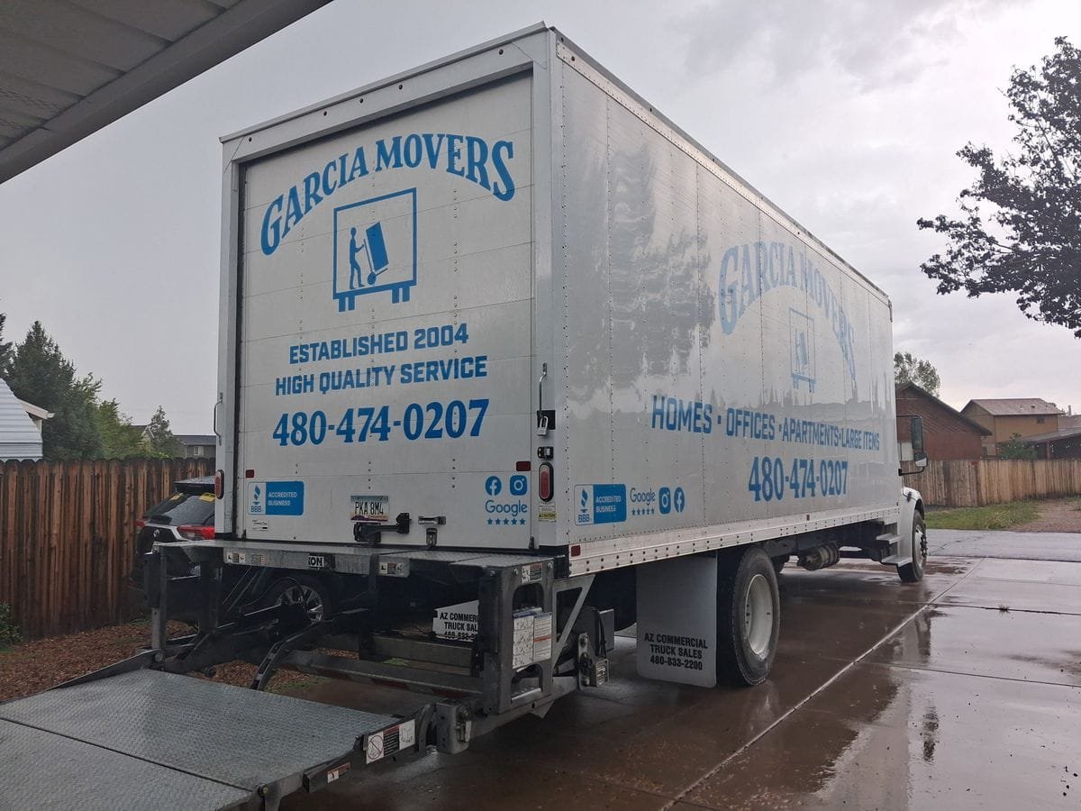 The back of a Garcia Movers truck with its lift gate down on a wet driveway