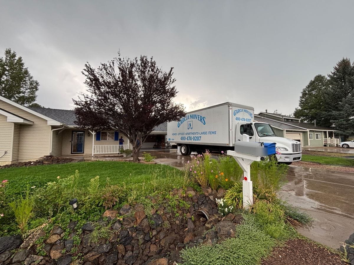 A Garcia Movers truck parked at a home on a rainy day, wildflowers in the front garden