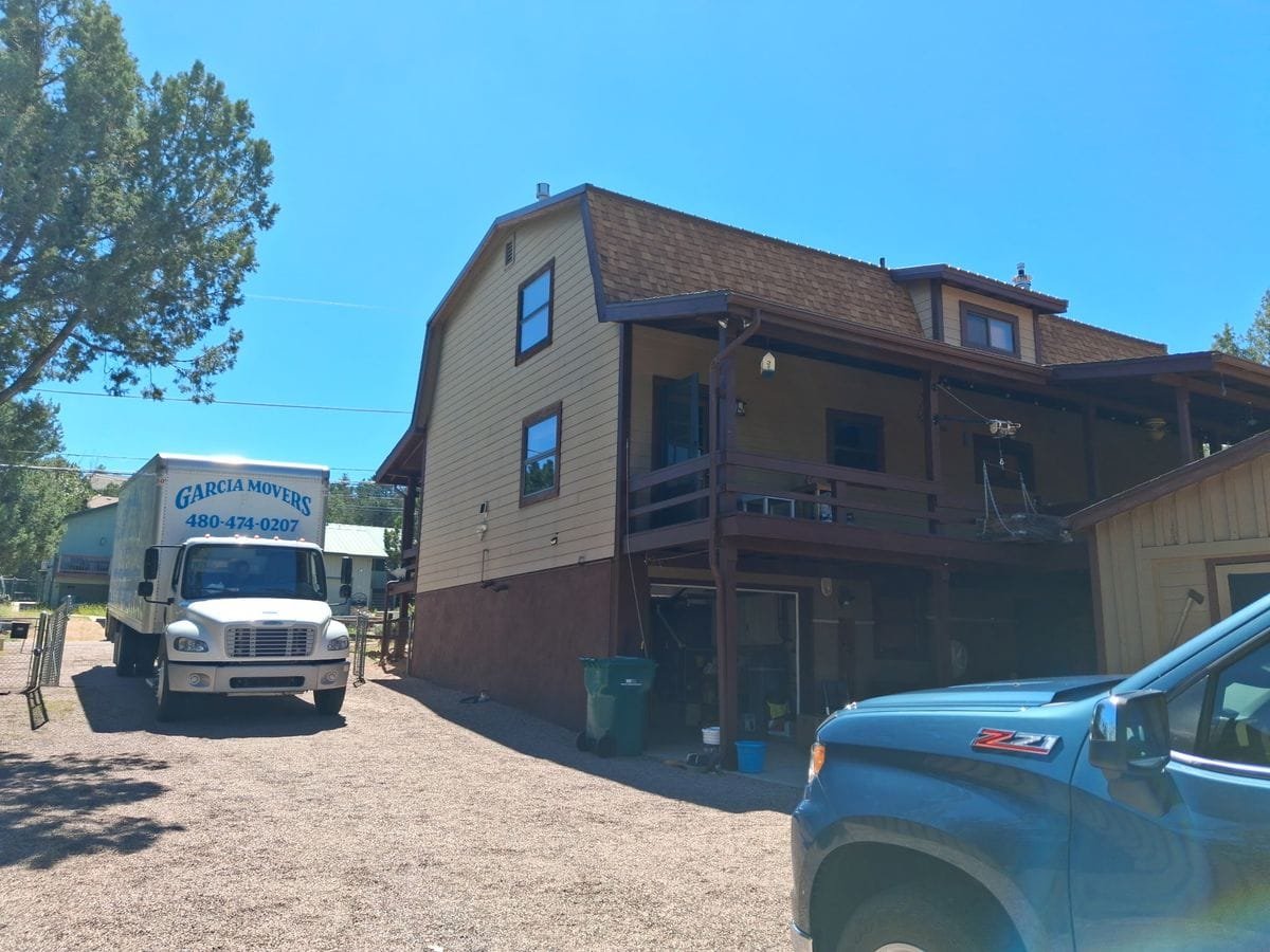 A Garcia Movers truck on a gravel drive beside a two-story home with a wraparound deck