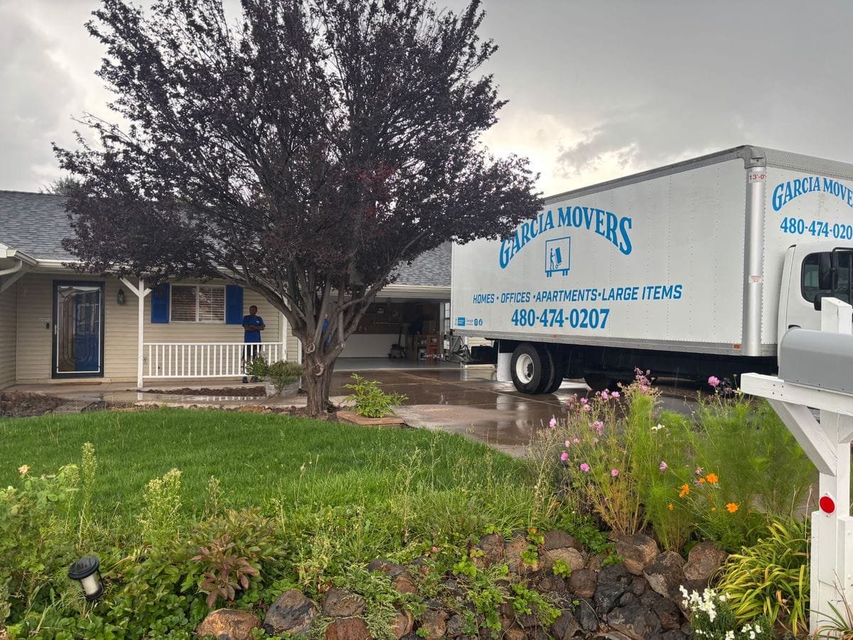 A Garcia Movers truck in a driveway behind a flowering tree under gray skies